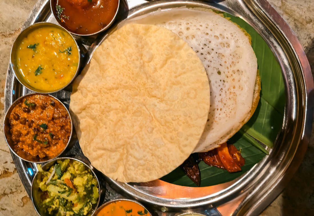 Thali with appam, papadum and small bowls of curry